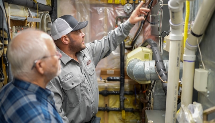 Hvac Technician Wtih Customer In Utility Room Looking At Furnace